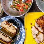 chicken and pork belly tacos topped with chunky cholula green chili sauce on a plate surrounded by pico de gallo and sliced cooked chicken.