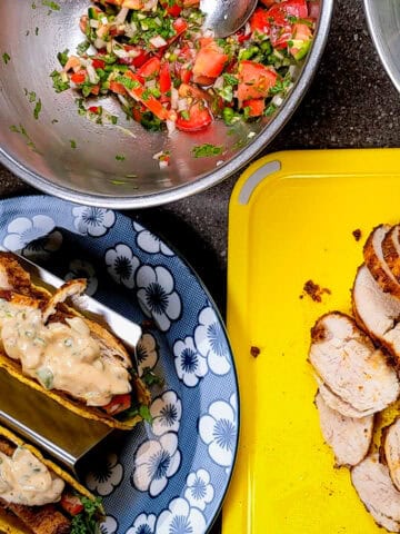 chicken and pork belly tacos topped with chunky cholula green chili sauce on a plate surrounded by pico de gallo and sliced cooked chicken.