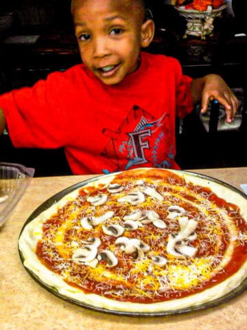 chef maika's son, jean garnishing a homemade pizza.