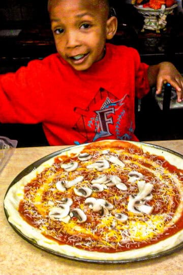 chef maika's son, jean garnishing a homemade pizza.