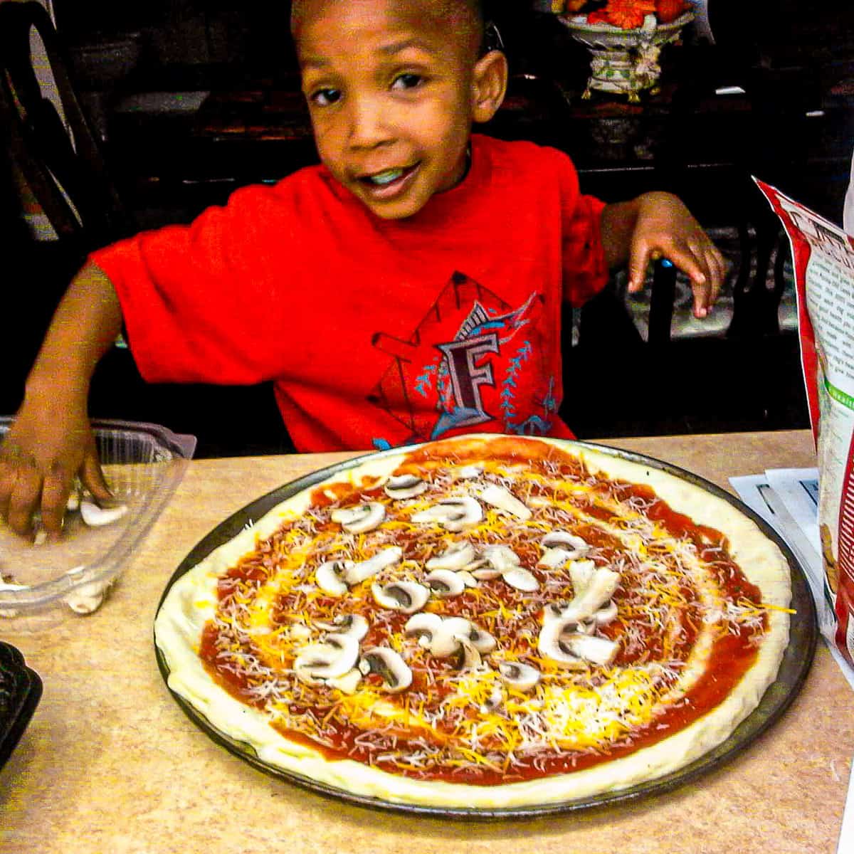 chef maika's son, jean garnishing a homemade pizza.