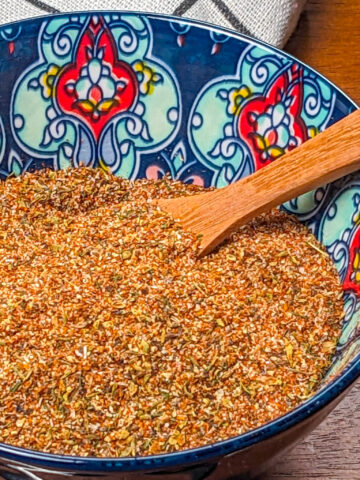all purpose steak seasoning in a decorated bowl with a wooden spoon.