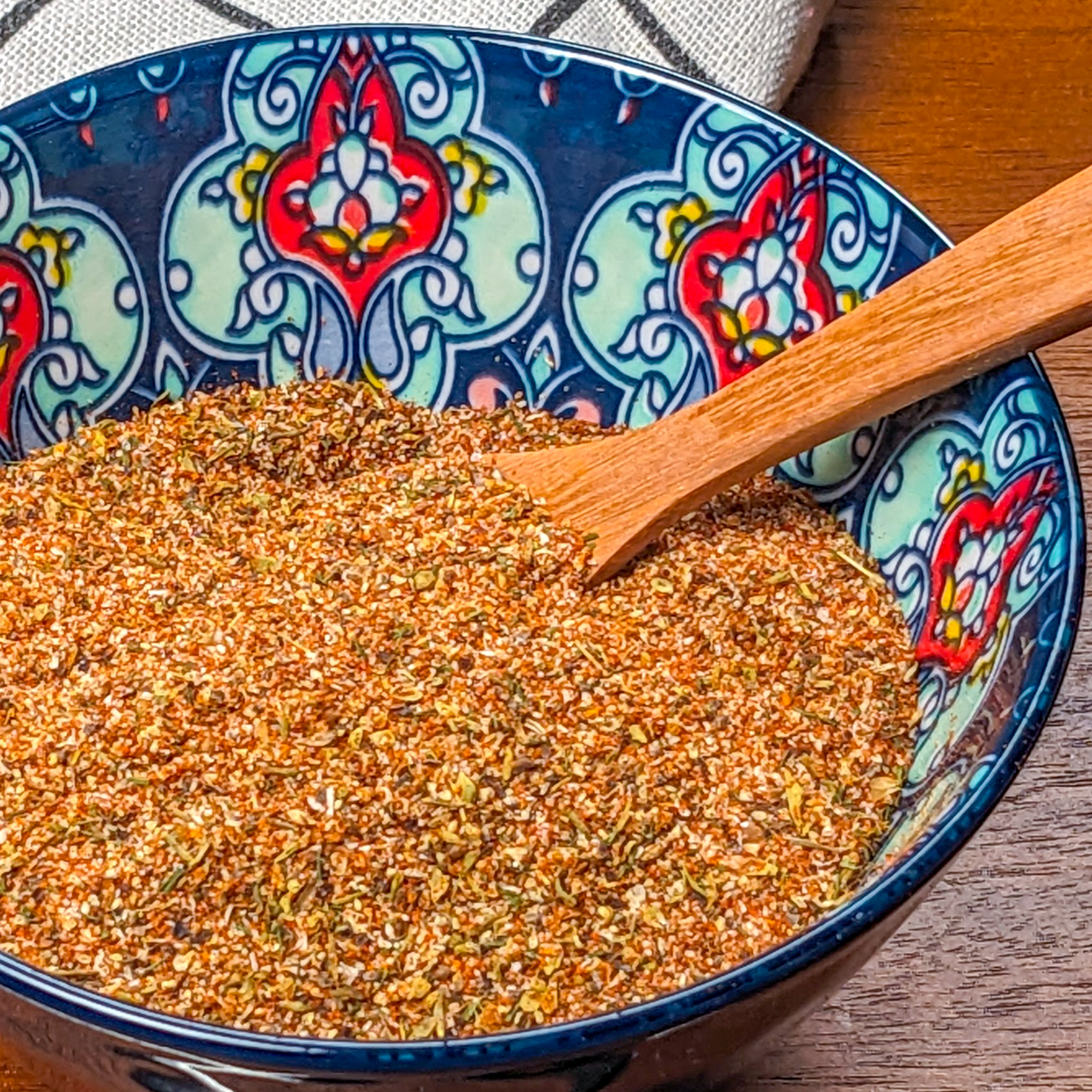 all purpose steak seasoning in a decorated bowl with a wooden spoon.