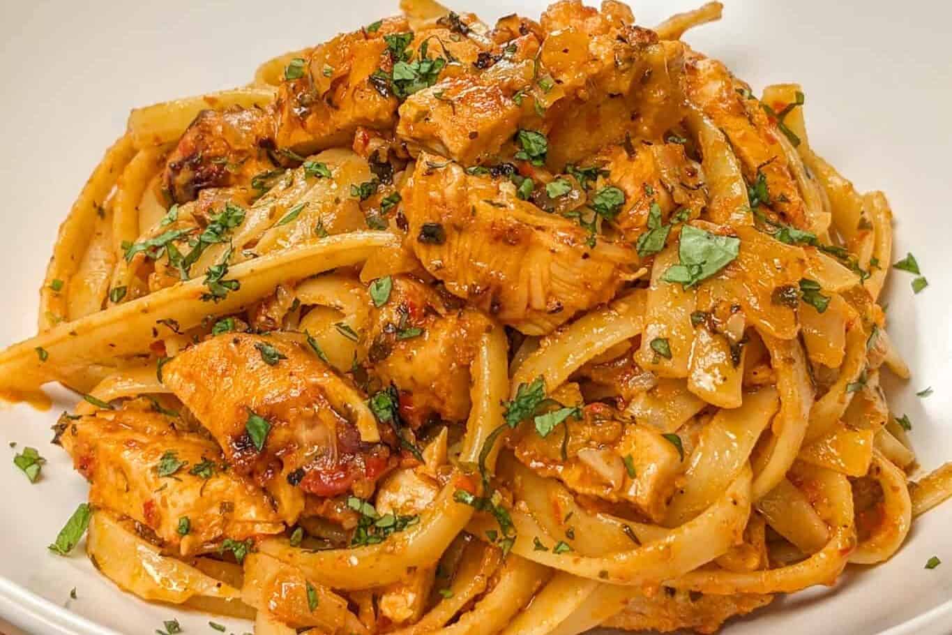 Simple Spicy Garlic Chili Sauce Chicken Pasta in a wide rim bowl with a kitchen towel and lodge enameled cast iron dutch oven with the remaining pasta dish in the background.