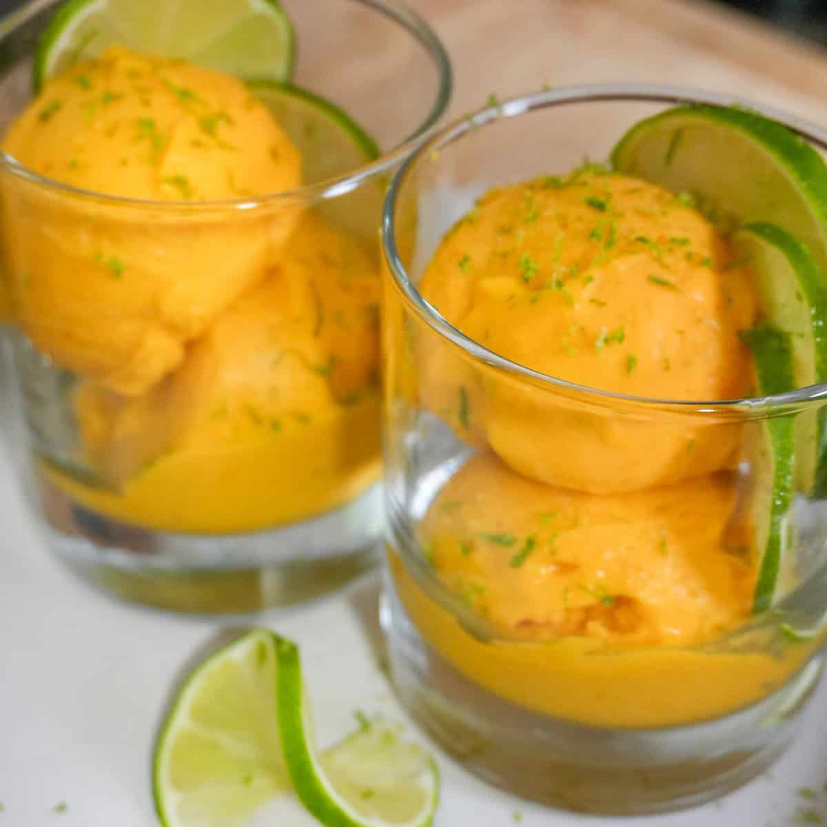 scooped mango coconut felato gelato in glass cups garnished with lime slices and lime zest.