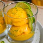 scooped mango coconut felato gelato in a glass cup garnished with lime slices and lime zest.
