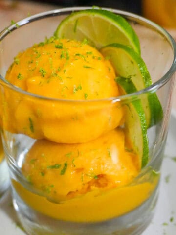 scooped mango coconut felato gelato in a glass cup garnished with lime slices and lime zest.