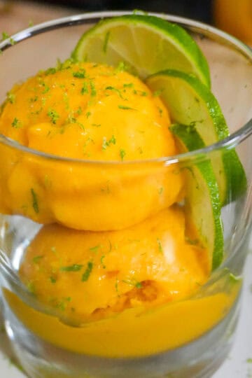 scooped mango coconut felato gelato in a glass cup garnished with lime slices and lime zest.