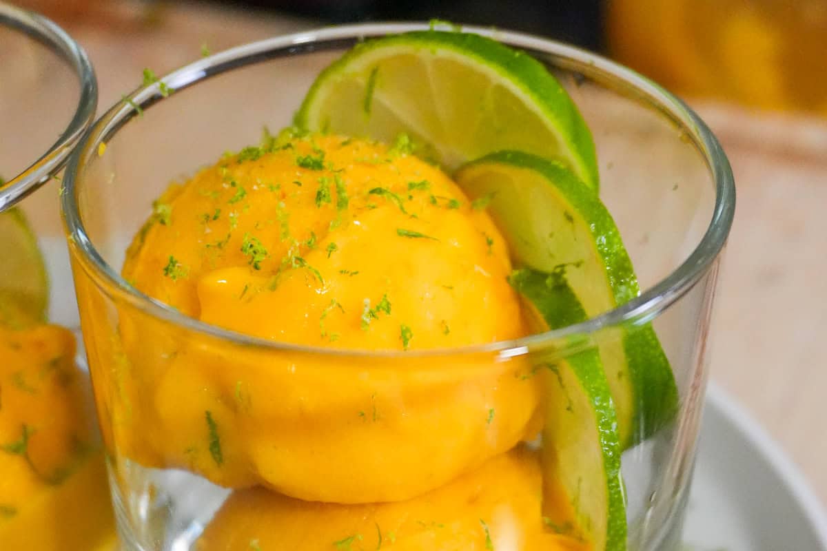scooped mango coconut felato gelato in a glass cup garnished with lime slices and lime zest.