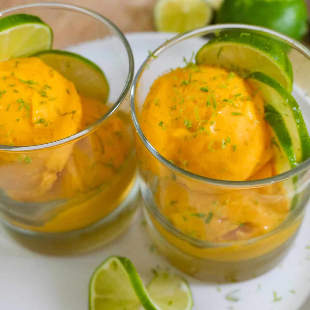 scooped mango coconut felato gelato in glass cups garnished with lime slices and lime zest.