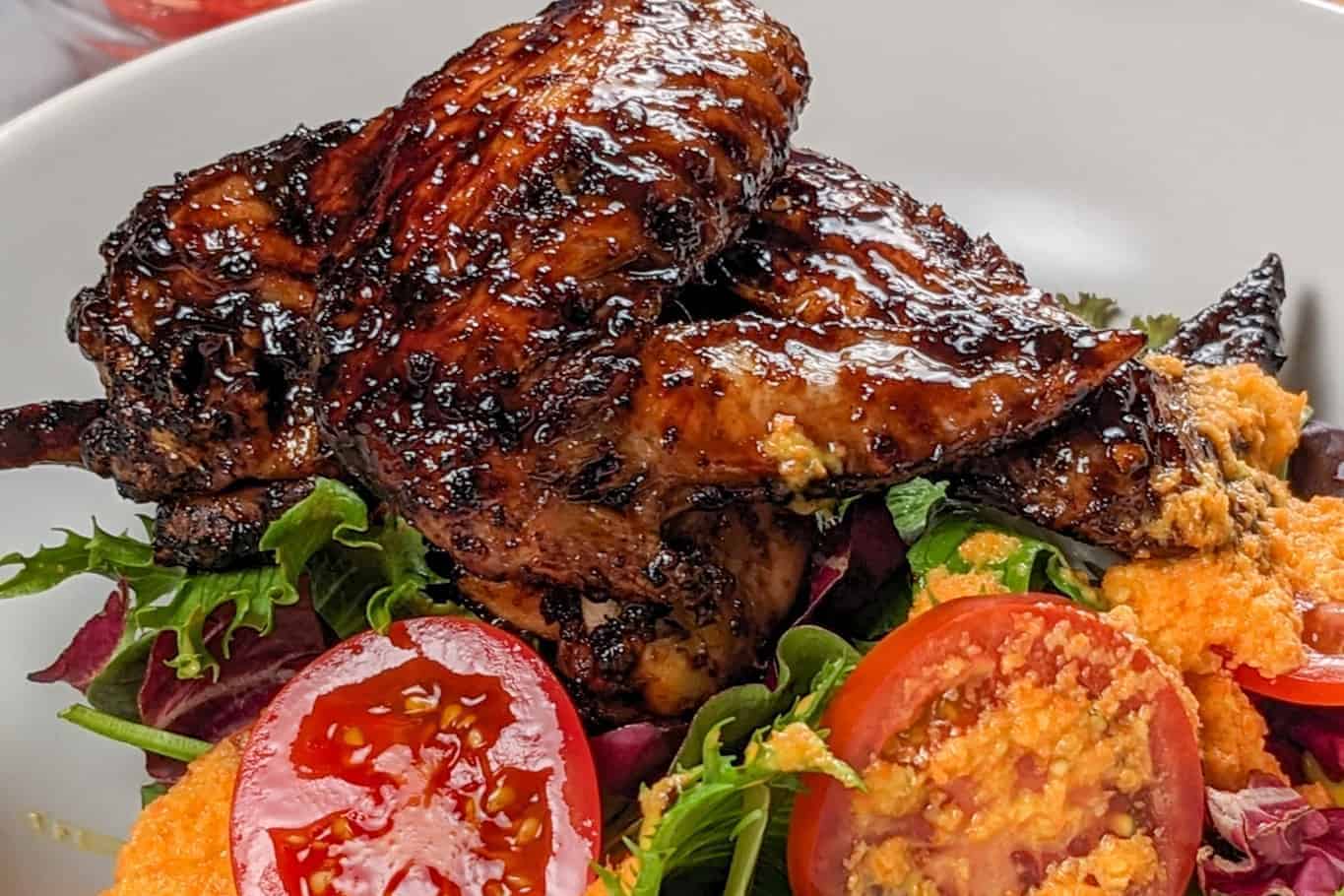 Side view of the Easy Air Fryer Sticky Date Teriyaki Chicken Wings next to mixed greens with sliced campari tomatoes and carrot ginger ddressing.