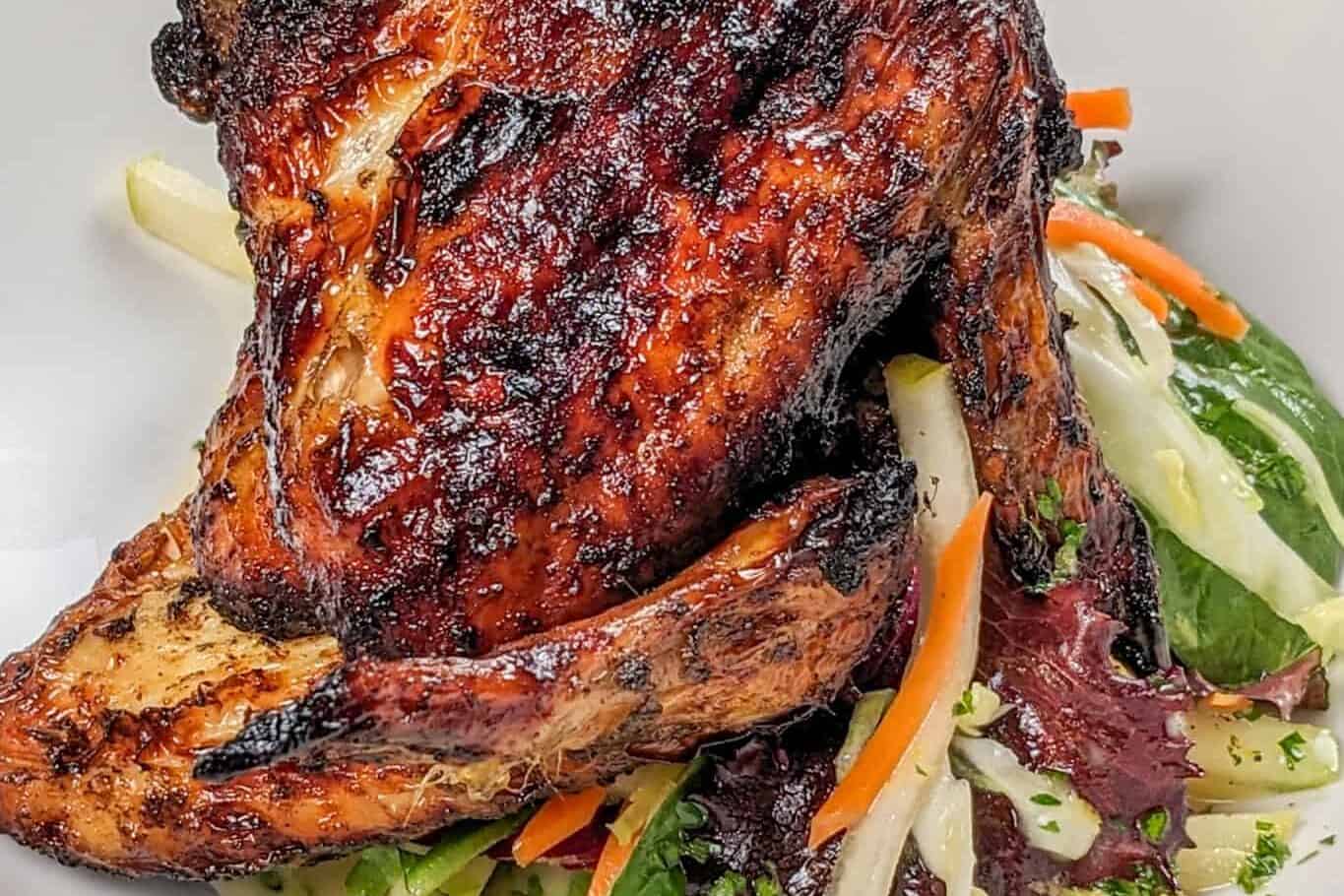 Side view of the Crispy Air Fryer Honey Jerk Rubbed Chicken Wings recipe next to marinated vegetables with greens and vinaigrette in a wide rim bowl
