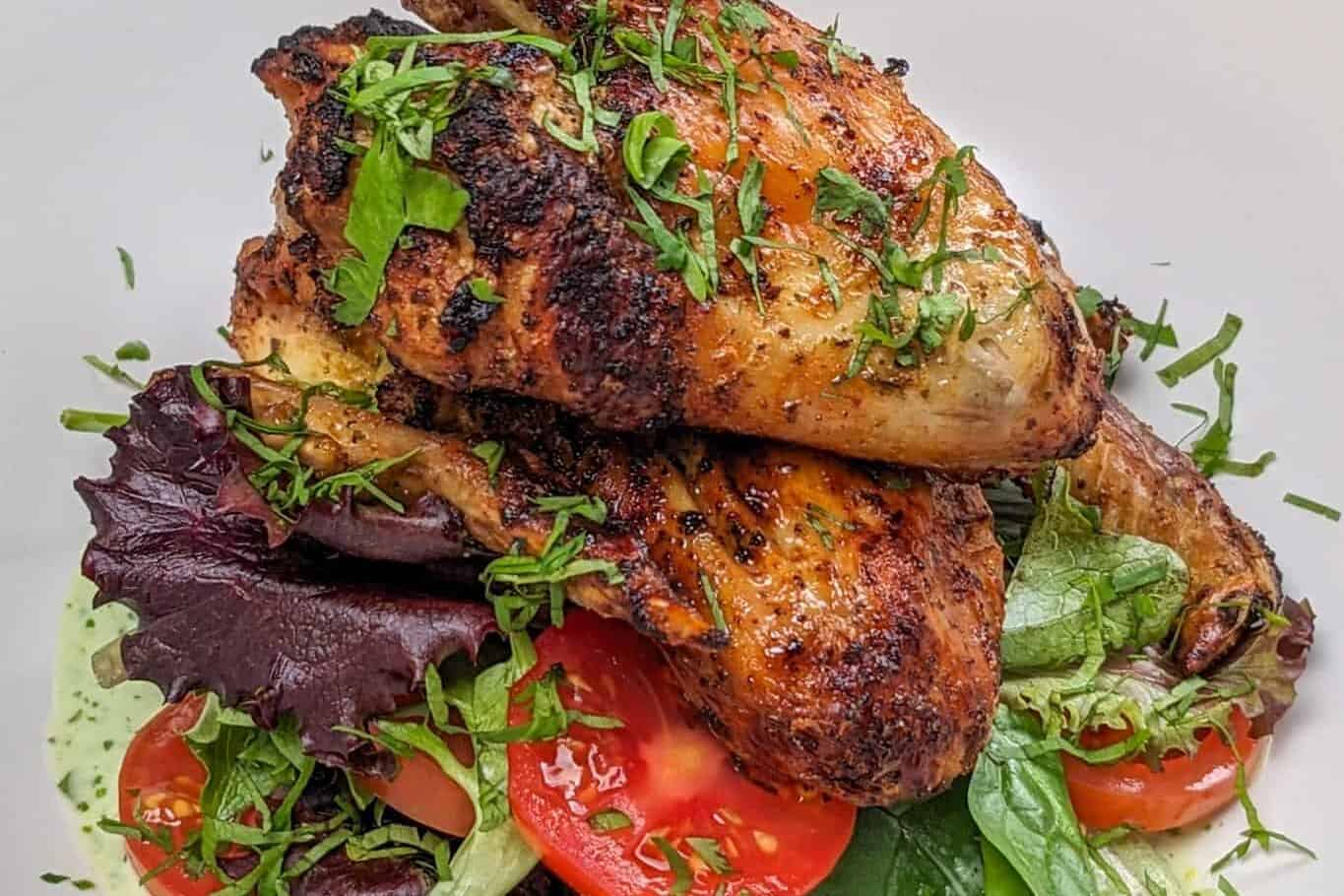 side view Plated Quick Air Fryer Lime Chicken Wings on greens with sliced campari tomatoes with Spicy Green Sauce on the bottom and the whole dish garnished with chiffonade herbs in a wide rim bowl