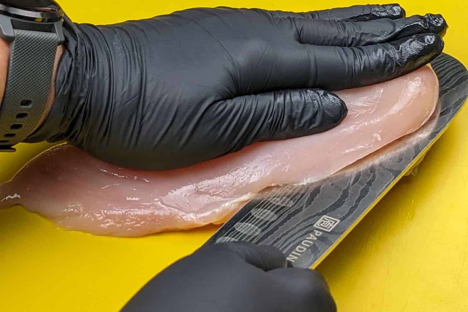 hands laid on the chicken breast to assist slicing the chicken breast horizontally.
