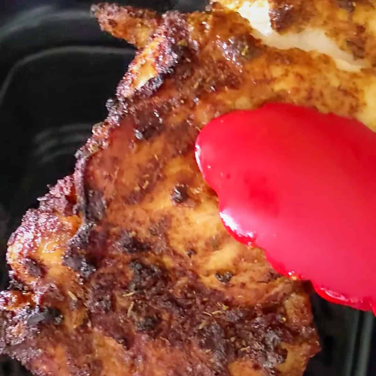 crispy air fried chicken breast held with tongs.