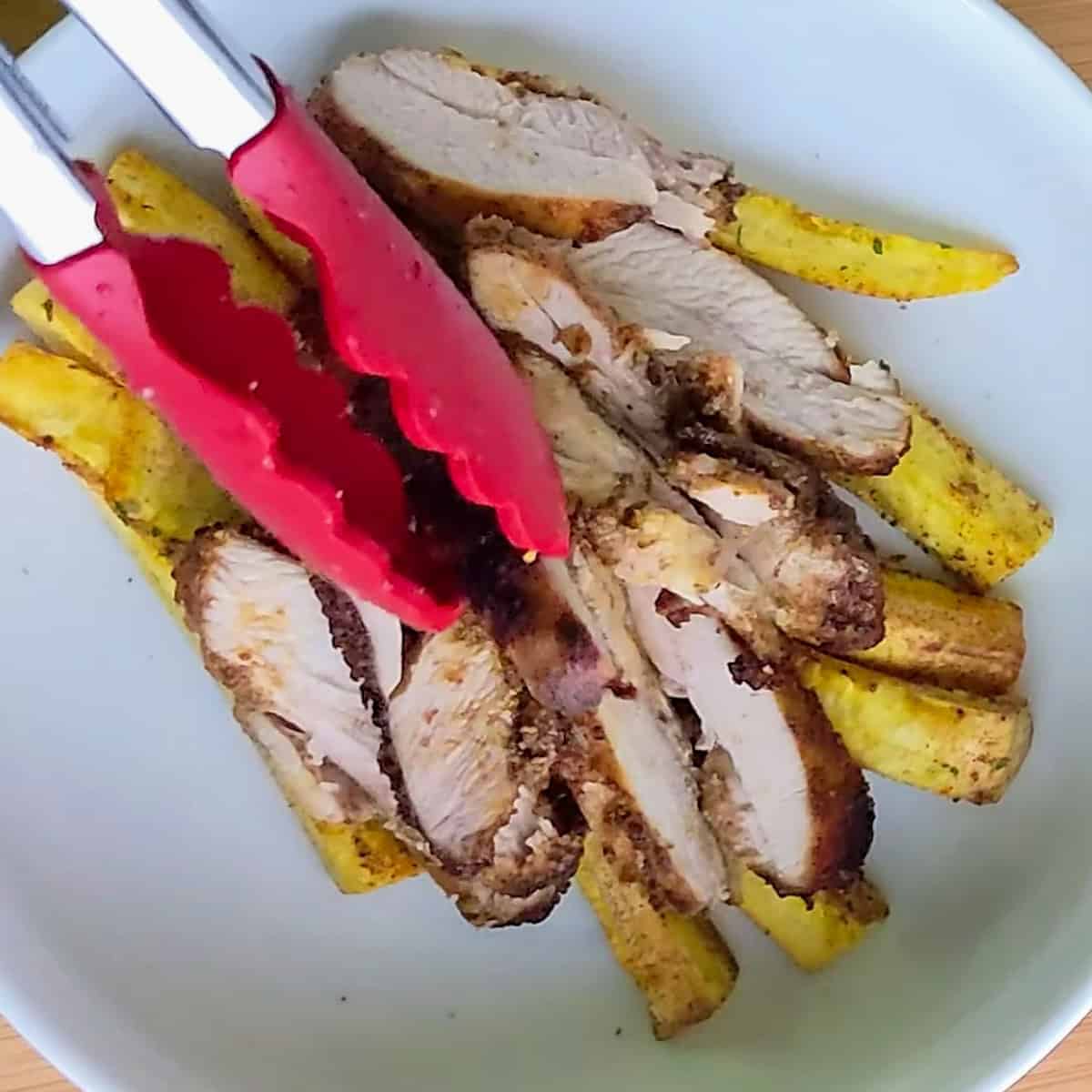 sliced adobo seasoned air fryer chicken placed on top of crispy plantain fries.
