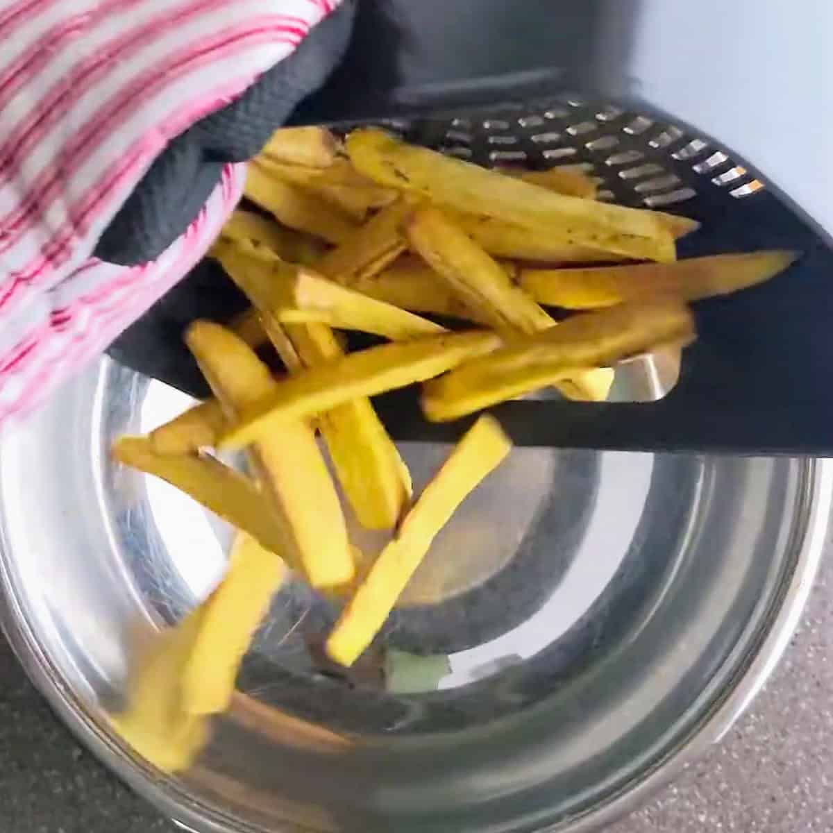 crisp plantain fries poured from the air fryer basket to mixing bowl.
