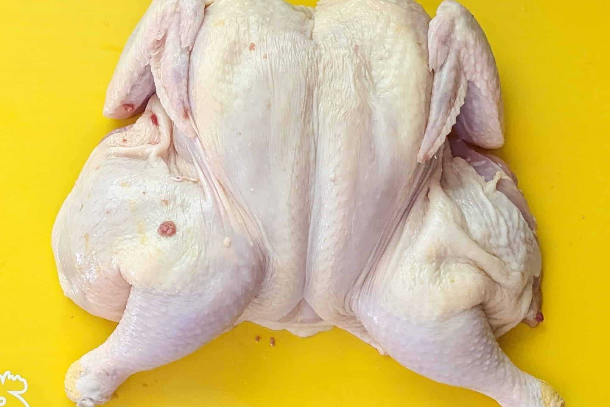 Finish product, a spatchcock chicken that has been flatten breast side up on a cutting board for poultry