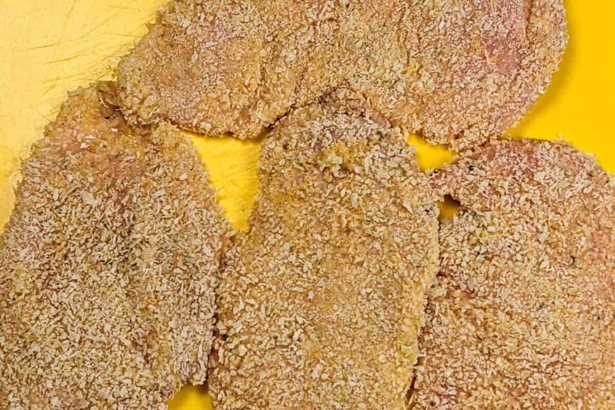 panko breaded chicken cutlets on a yellow cutting board mat.