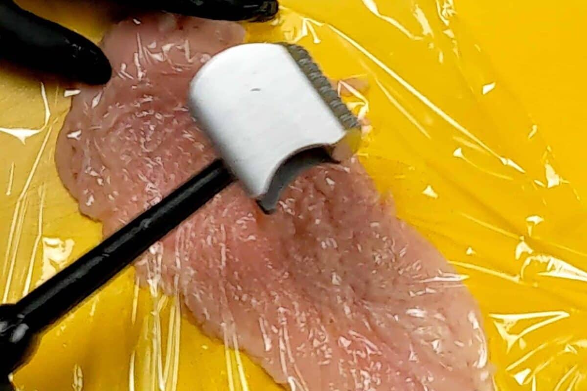 halved chicken being pounded out with a meat mallet on a yellow cutting board