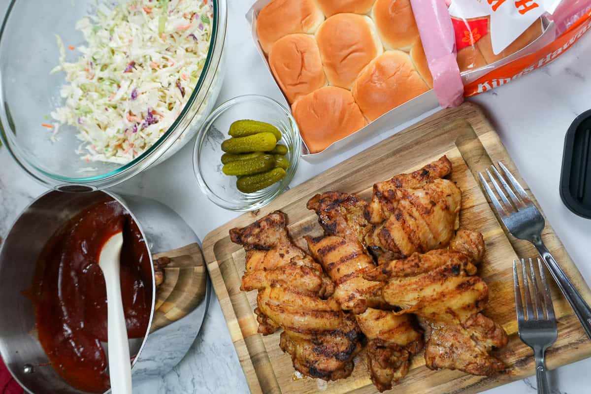 everything to assemble the bbq chicken sliders, grilled chicken, bbq sauce, coleslaw, dill pickles, and hawaiin sweet rolls.