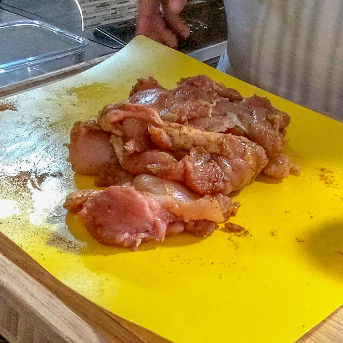 seasoned chicken thighs on a color coded cutting board mat for raw poultry.