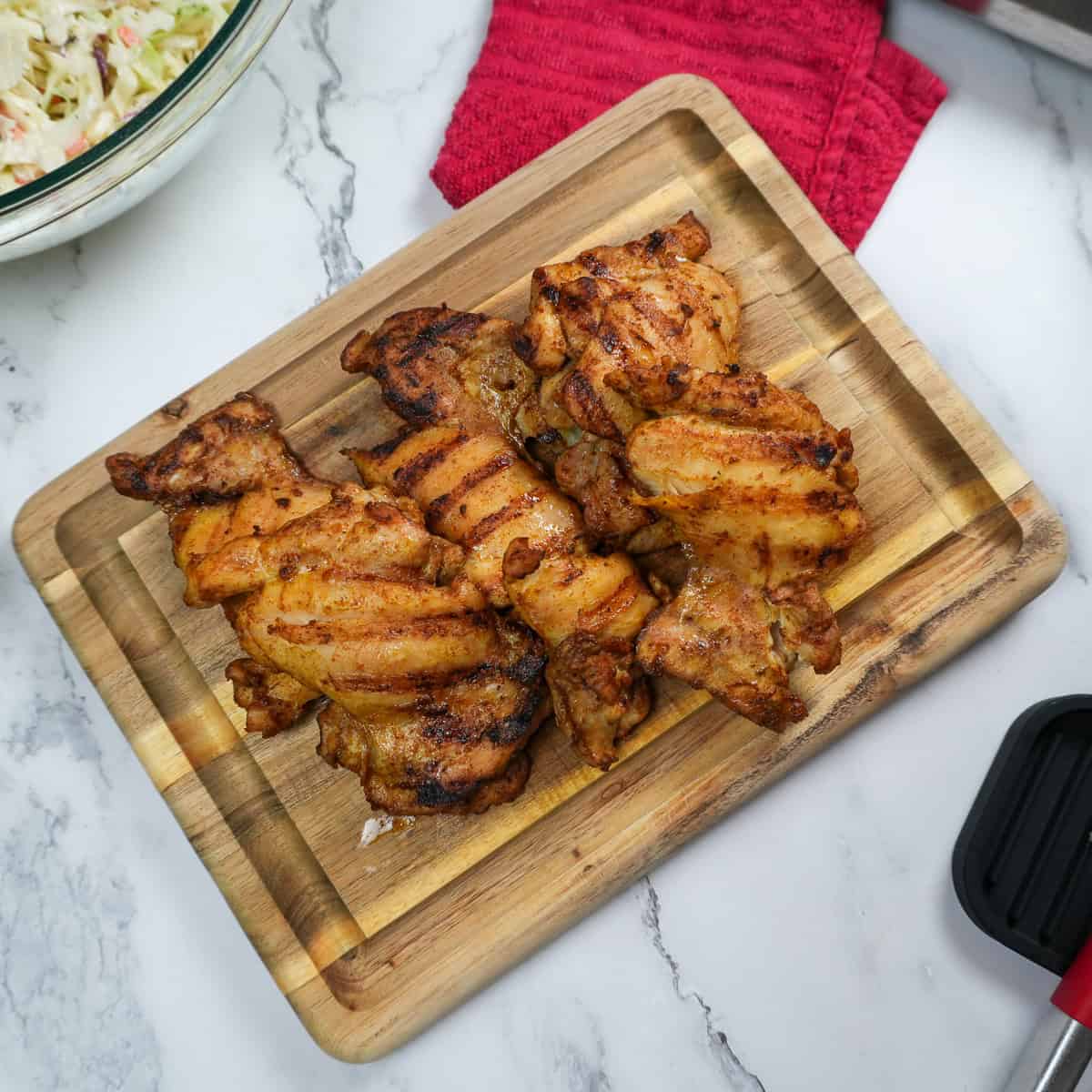 grilled chicken resting on a wooden cutting board.