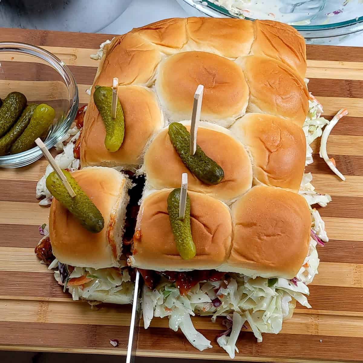 bbq chicken sliders with coleslaw skewered with bamboo skewers and miniature whole dill pickles.