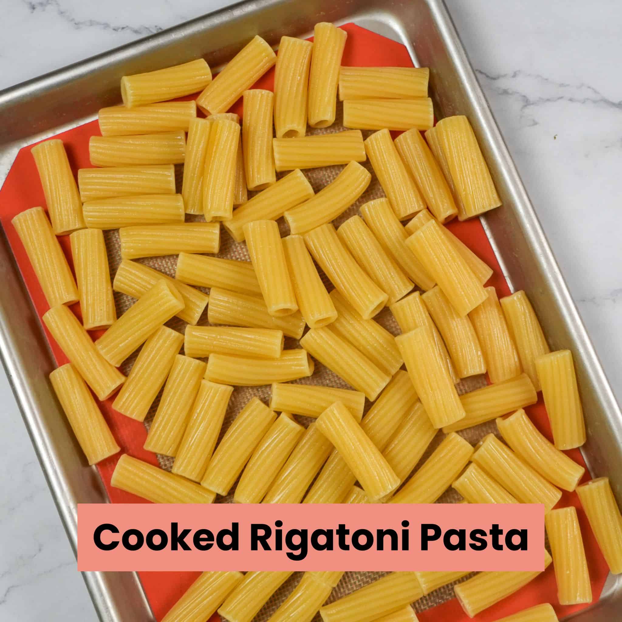 cooked rigatoni pasta on a silicone lined sheet pan.