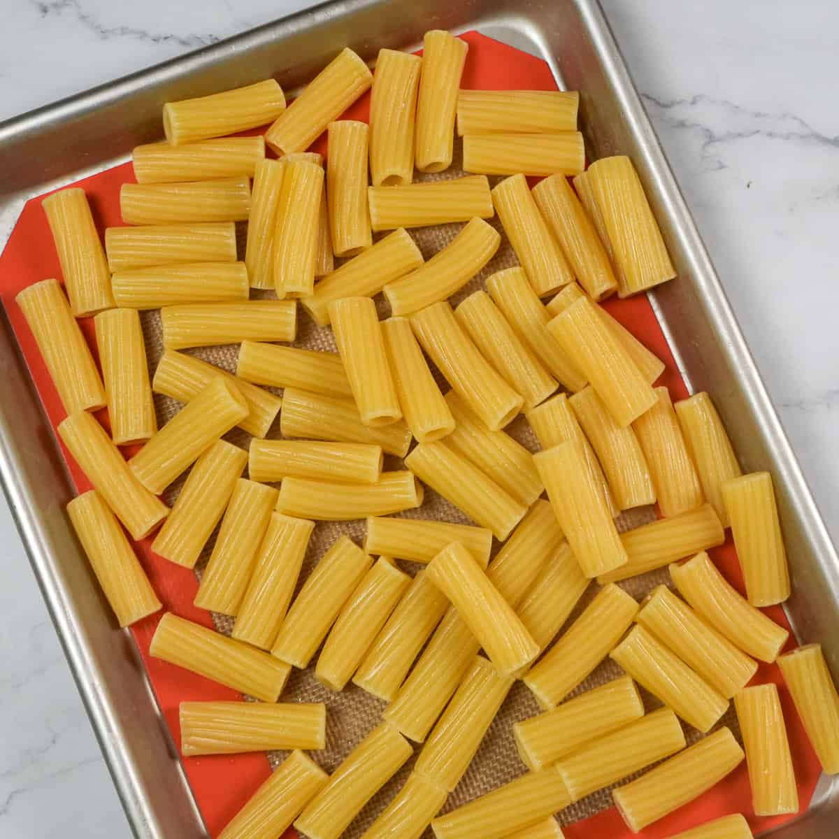 cooked rigatoni pasta on a silicone lined sheet pan.