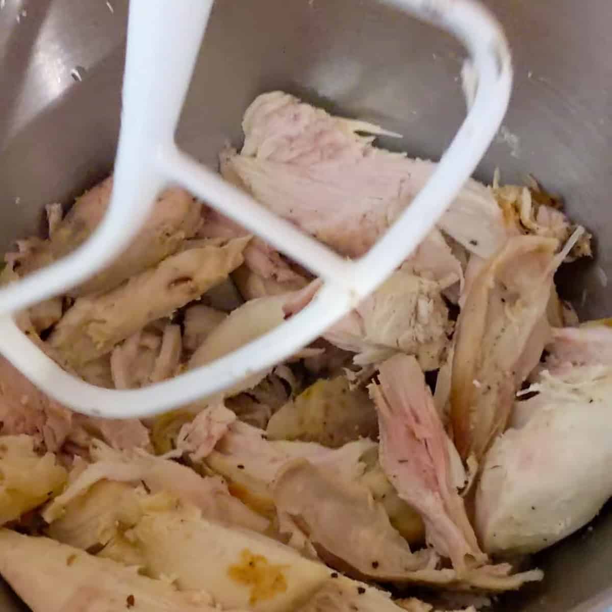 rotisserie chicken pieces in a kitchenaid stand mixer with a paddle attachment.