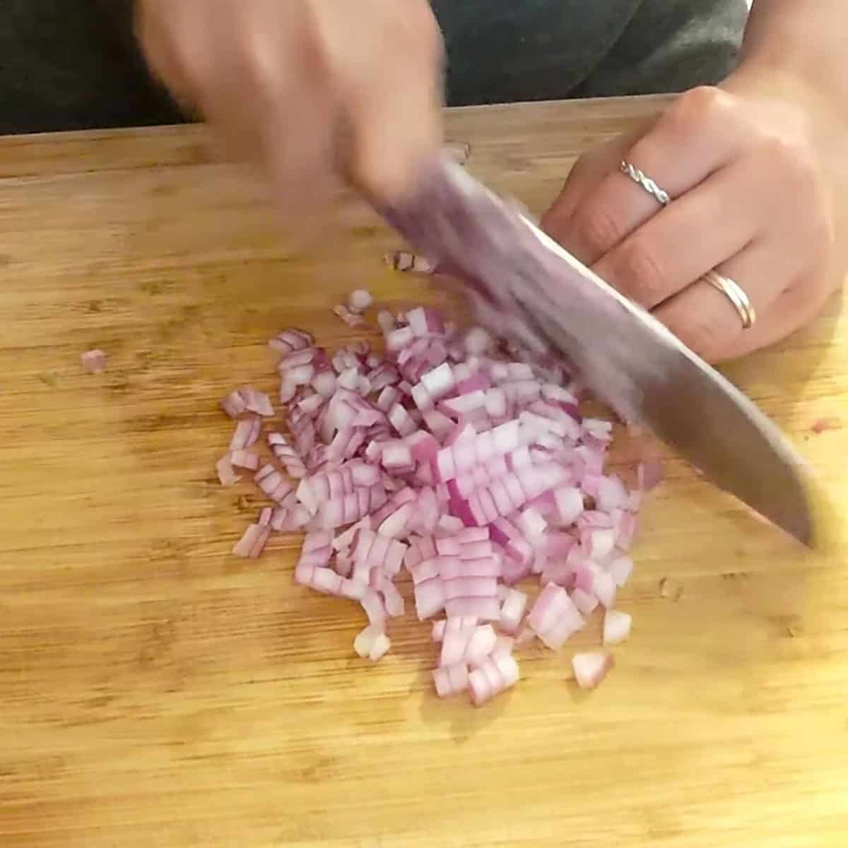 fine dicing red onion on a wooden cutting board.