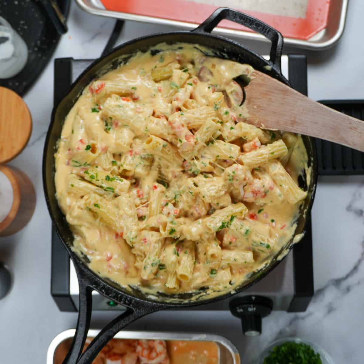 shrimp mac and cheese being mixed with a wooden spoon in a cast iron skillet.