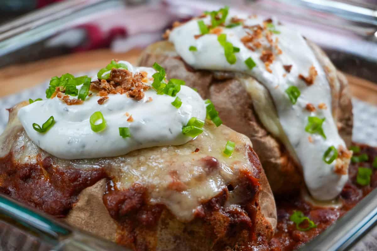 close up of the turkey chili baked potatoes topped with seasoned sour cream, chopped scallion and fried shallots in a glass baking dish.