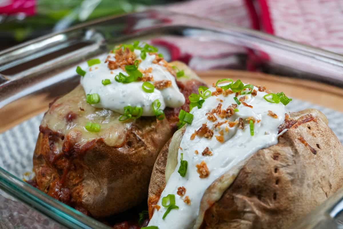 close up of the turkey chili baked potatoes topped with seasoned sour cream, chopped scallion and fried shallots in a glass baking dish.