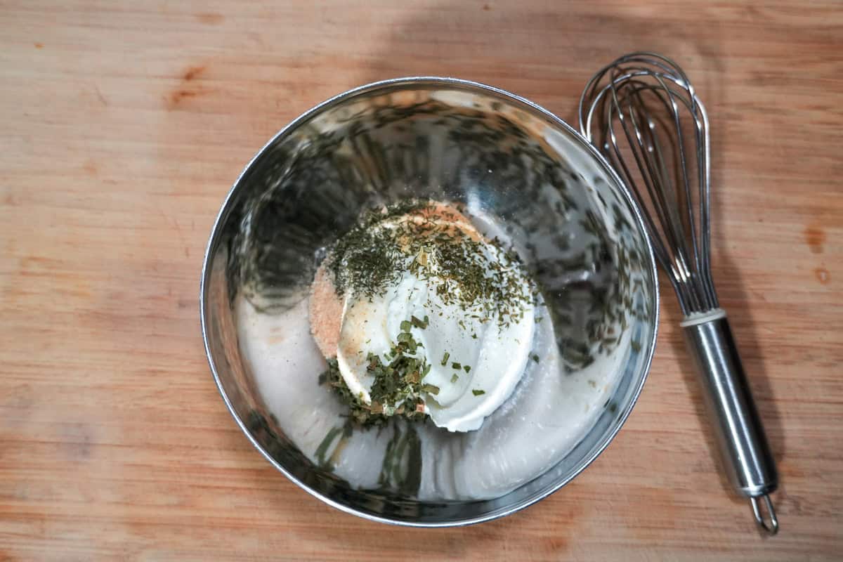 ingredients for the sour cream chive topping mixture in a bowl with a mini whisk resting next to it.