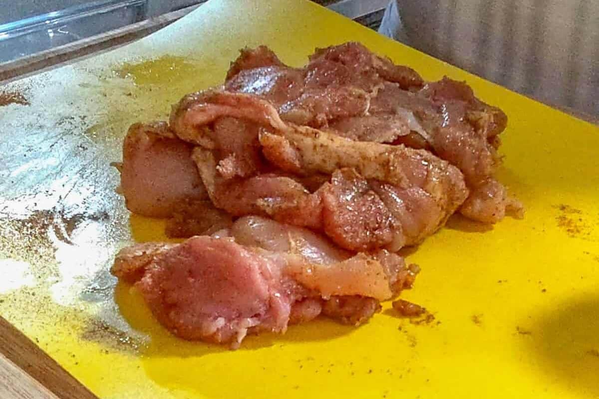 seasoned chicken thighs on a color coded cutting board mat for raw poultry.
