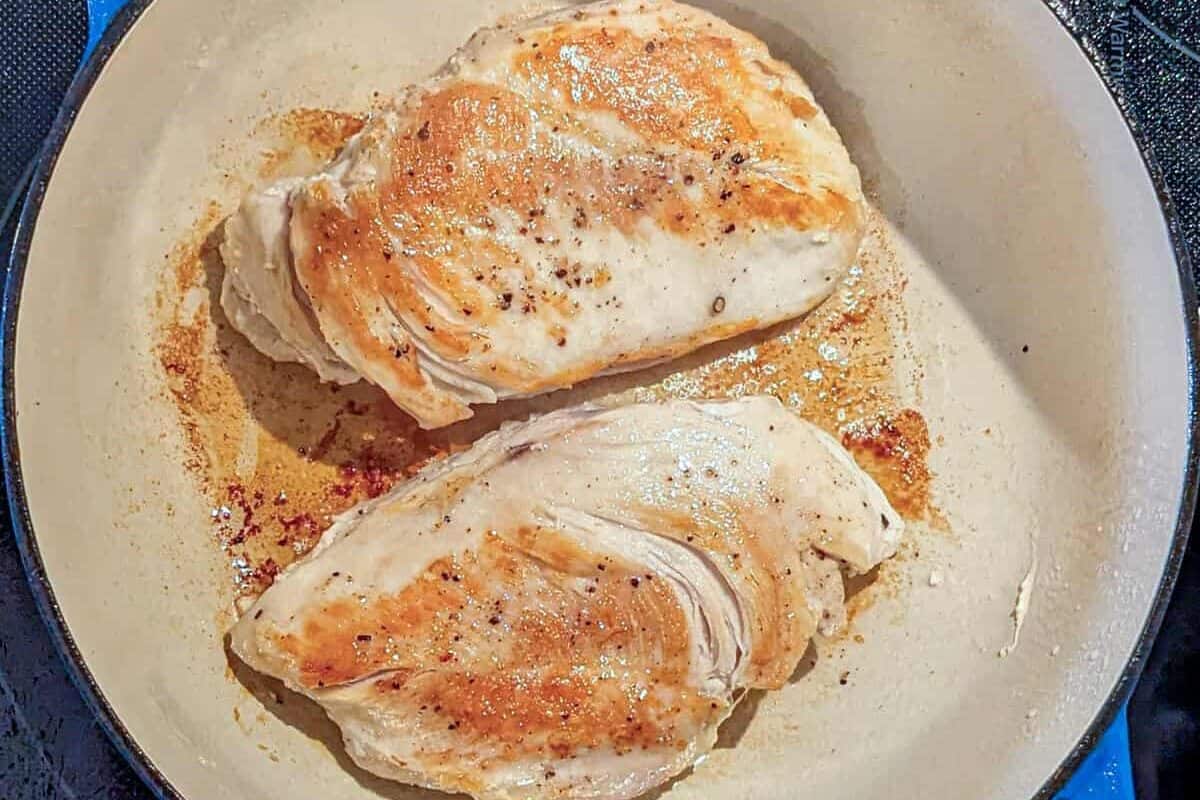 Golden-brown chicken breasts searing in a cast-iron skillet for a delicious Curry Coconut Soup.