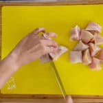 cutting chicken breast into large chunks on a cutting mat for raw poultry.
