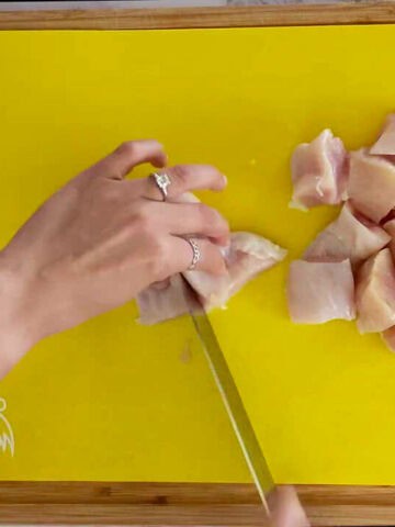 cutting chicken breast into large chunks on a cutting mat for raw poultry.