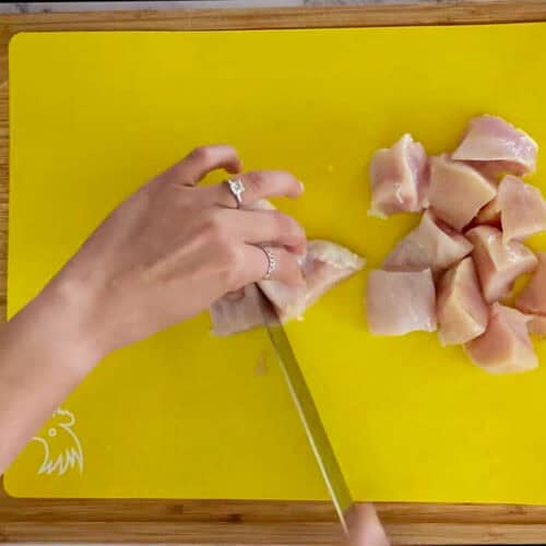 cutting chicken breast into large chunks on a cutting mat for raw poultry.