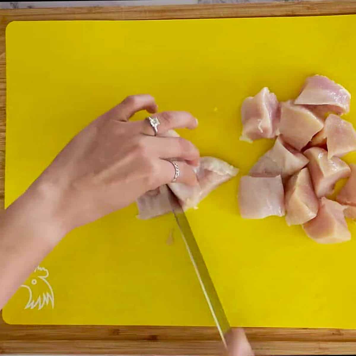 cutting chicken breast into large chunks on a cutting mat for raw poultry.