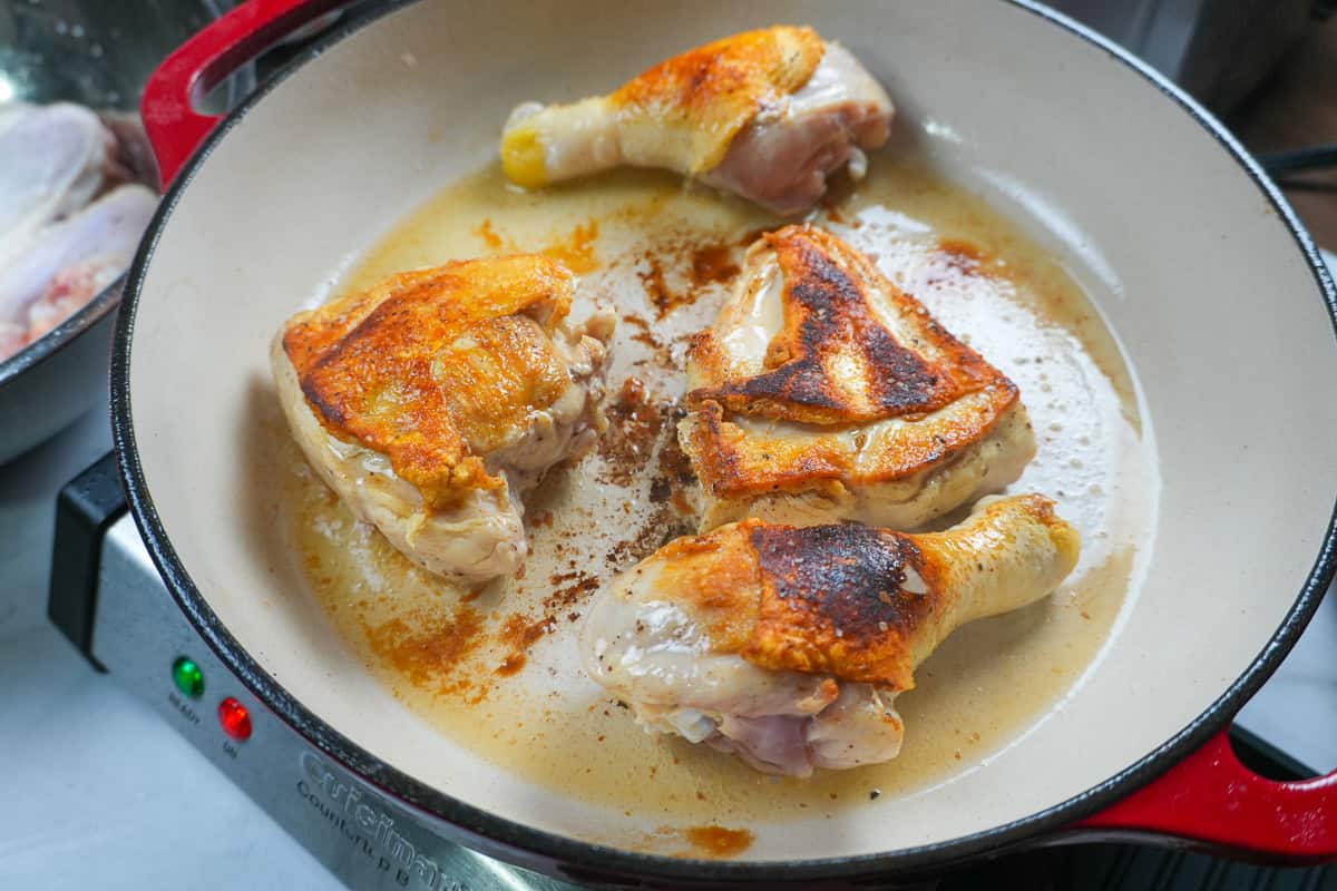 seared bone-in skin-on chicken pieces in an enameled dutch oven with olive oil.