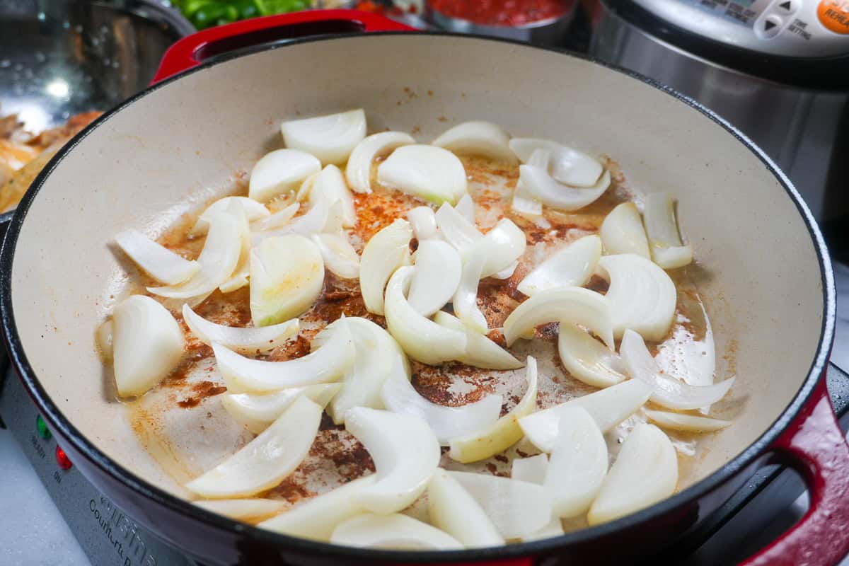 raw sliced onions in a dutch oven on the fond of the seared chicken.