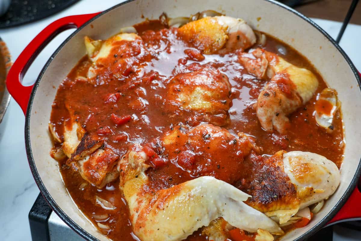 sauce poured onto browned chicken pieces in a dutch oven.