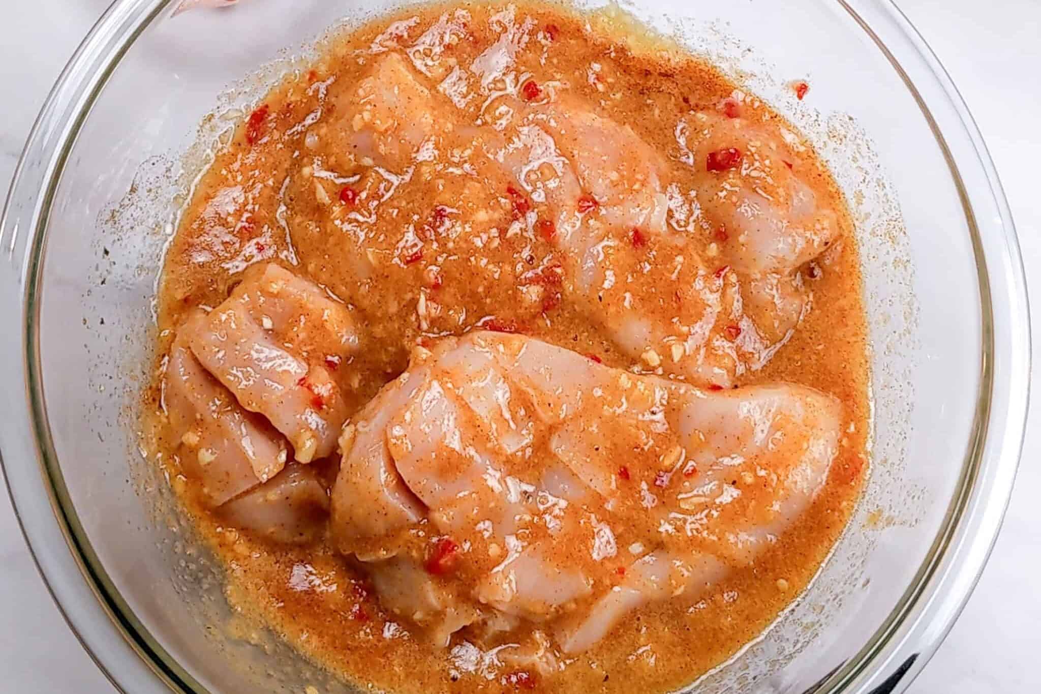 peach piri piri chicken marinating in a glass mixing bowl.