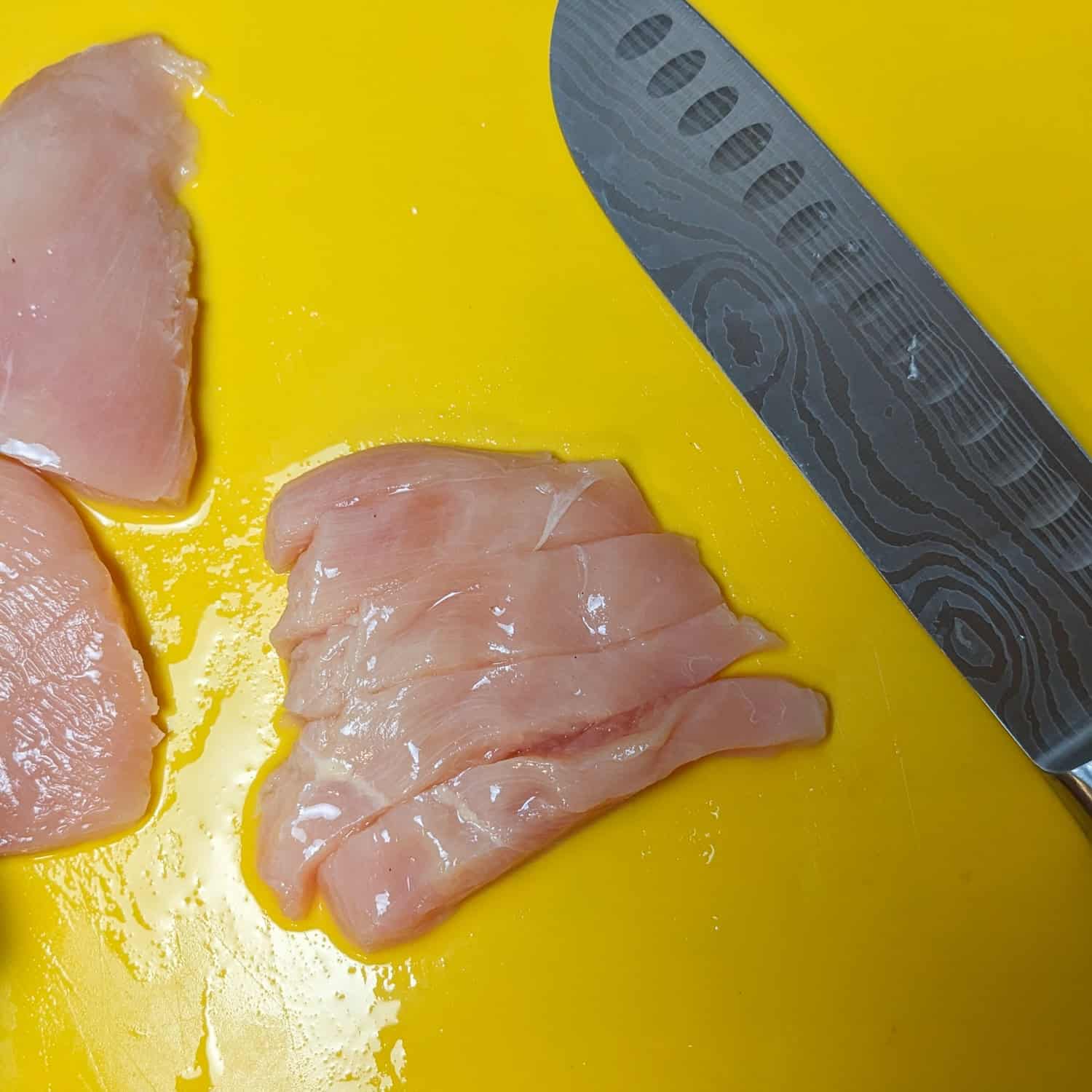 quarter of chicken breast cut into slices on a yellow cutting board near a knife.