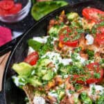 nachos topped with fresh avocado, tomatoes, sour cream and cilantro in a Lodge Cast Iron Skillet.