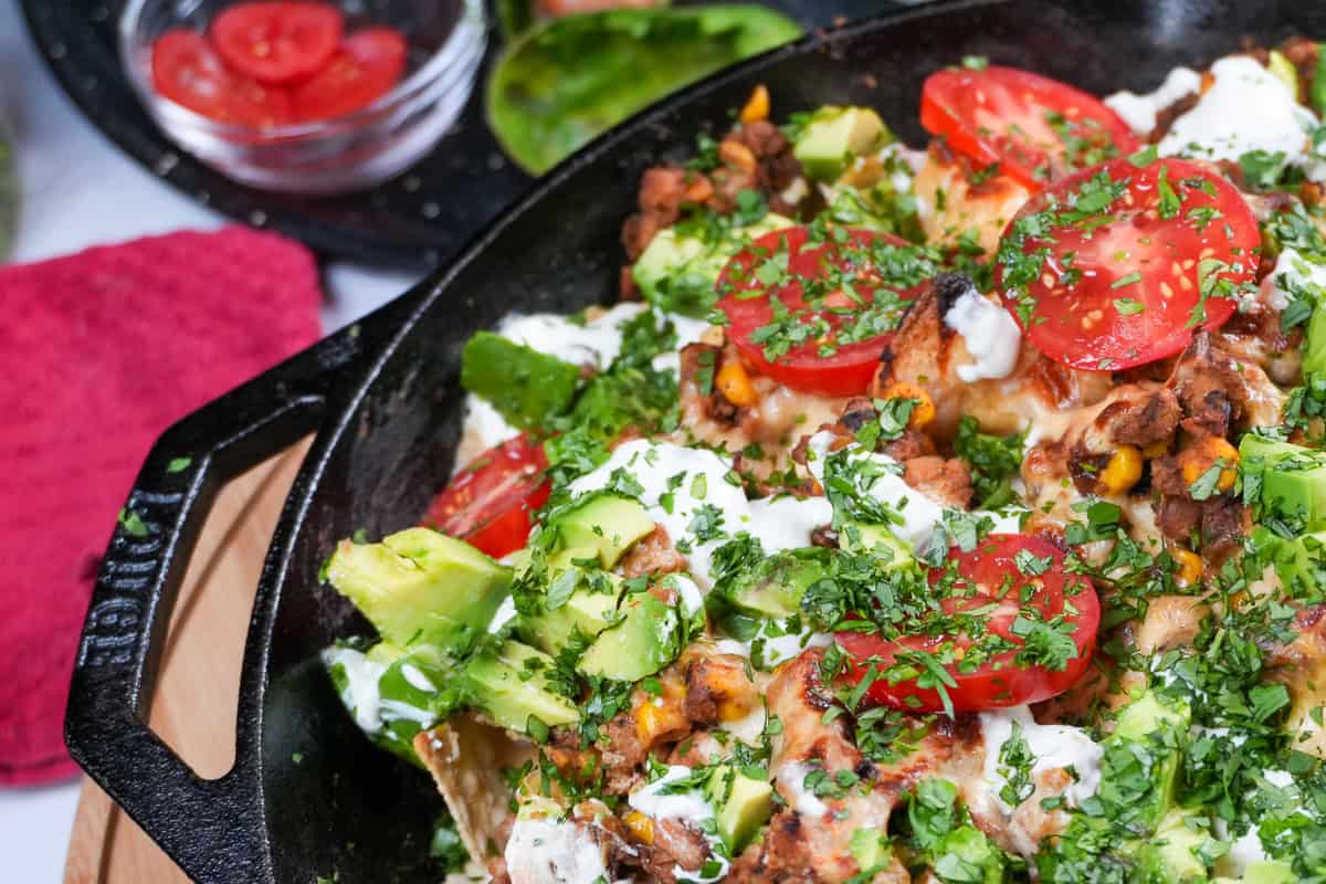 nachos topped with fresh avocado, tomatoes, sour cream and cilantro in a Lodge Cast Iron Skillet.