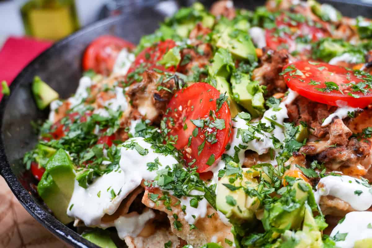 nachos topped with fresh avocado, tomatoes, sour cream and cilantro in a Lodge Cast Iron Skillet.